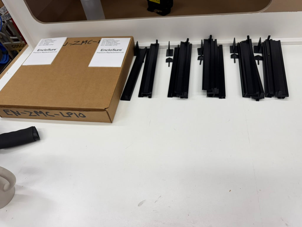 Multiple EncloSure lids laid out across the JW Designs laser workbench.